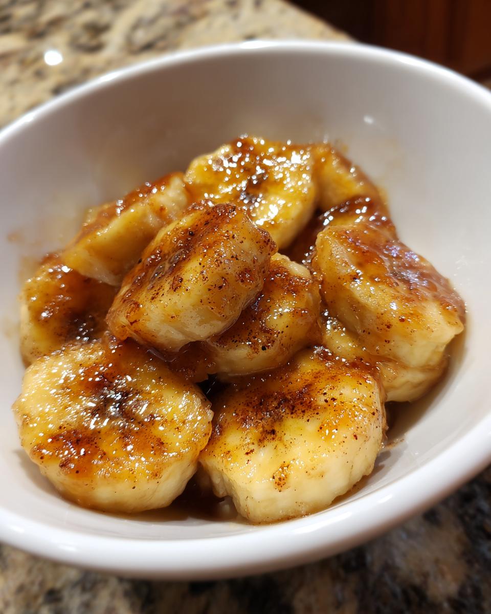 Close-up of caramelized banana dessert bites coated in glaze in a white bowl.