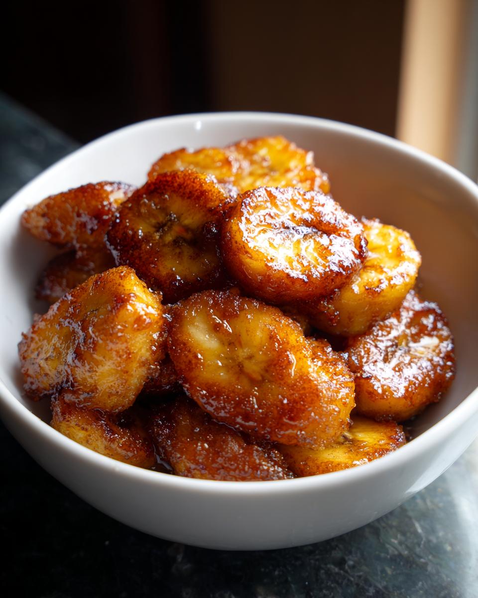 Close-up of caramelized banana dessert bites with a golden glaze in a white bowl.