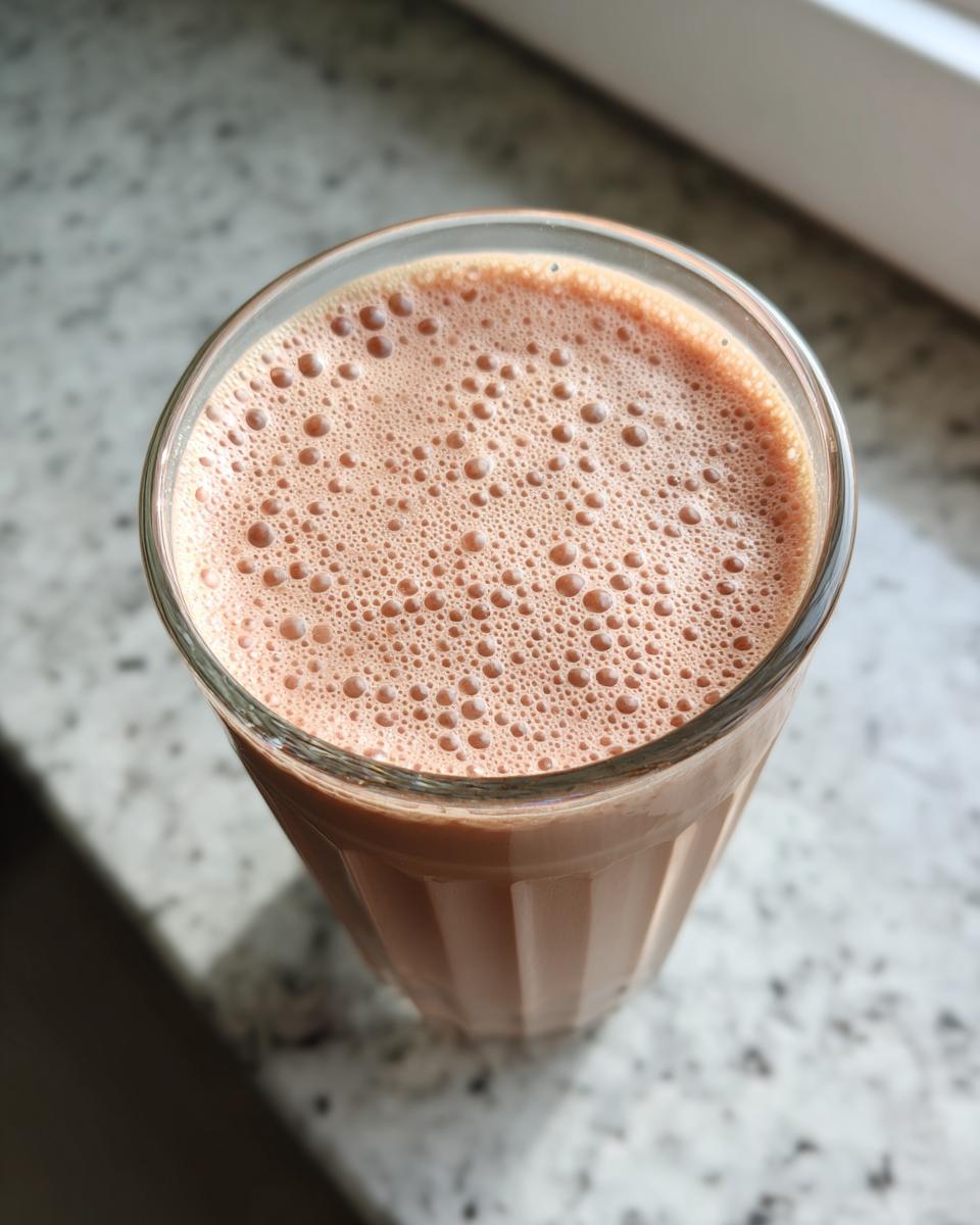 Close-up of a chocolate protein breakfast smoothie with bubbles in a clear glass.