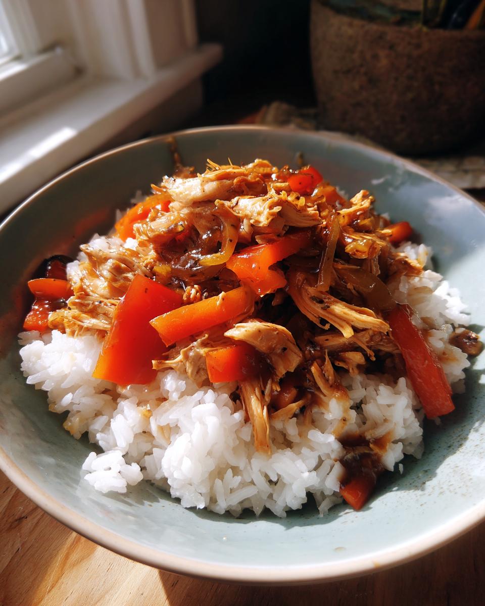Bowl of white rice topped with shredded chicken, red bell peppers, and sauce for easy rice bowl dinners.