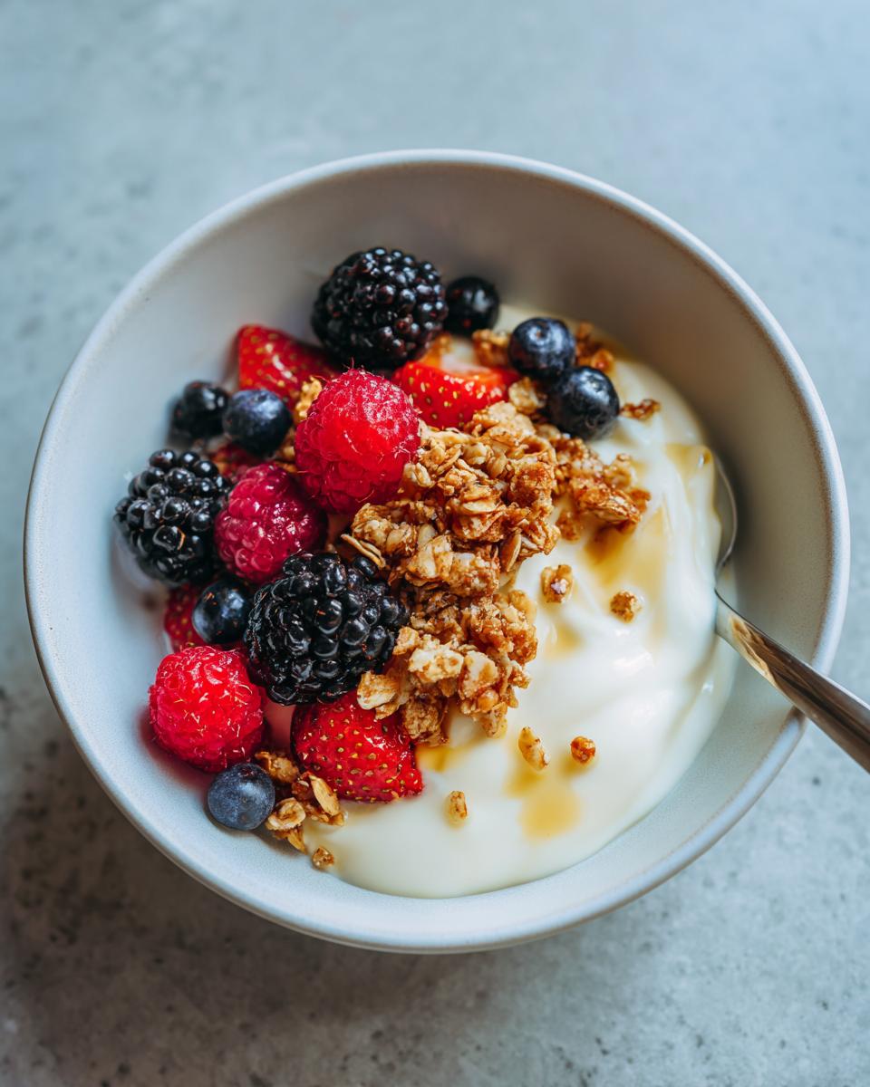 Bowl of easy yogurt dessert recipes topped with fresh berries, granola, and honey drizzle.