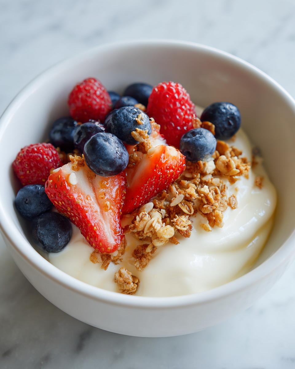 Bowl of easy yogurt dessert recipes topped with strawberries, blueberries, raspberries, and granola