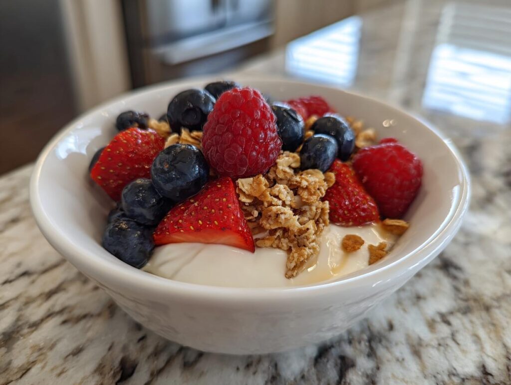 Bowl of yogurt topped with fresh strawberries, blueberries, raspberries, and granola