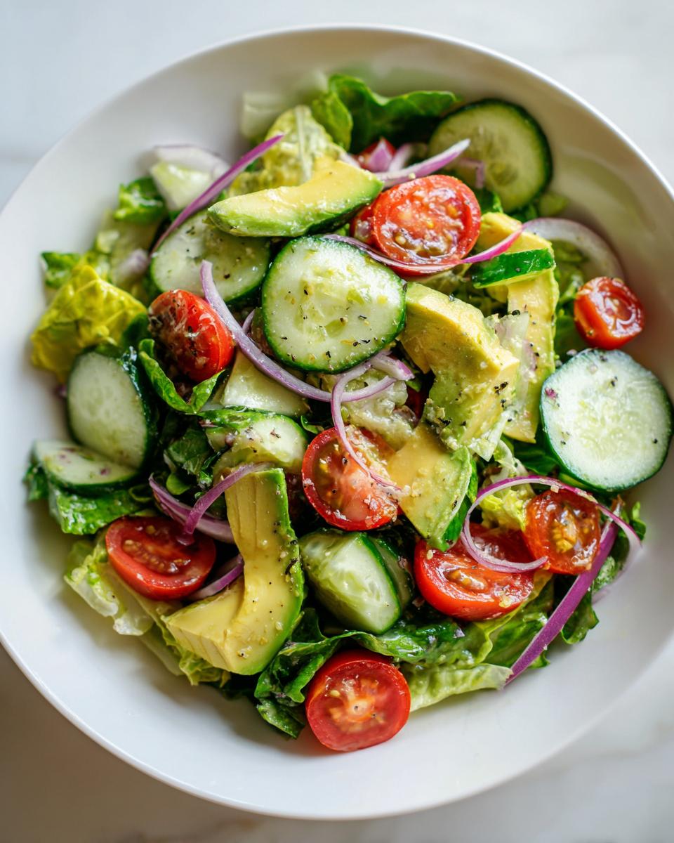 Bowl of fresh salad with avocado, cherry tomatoes, cucumber, red onion, and lettuce, an easy side dish salad recipes
