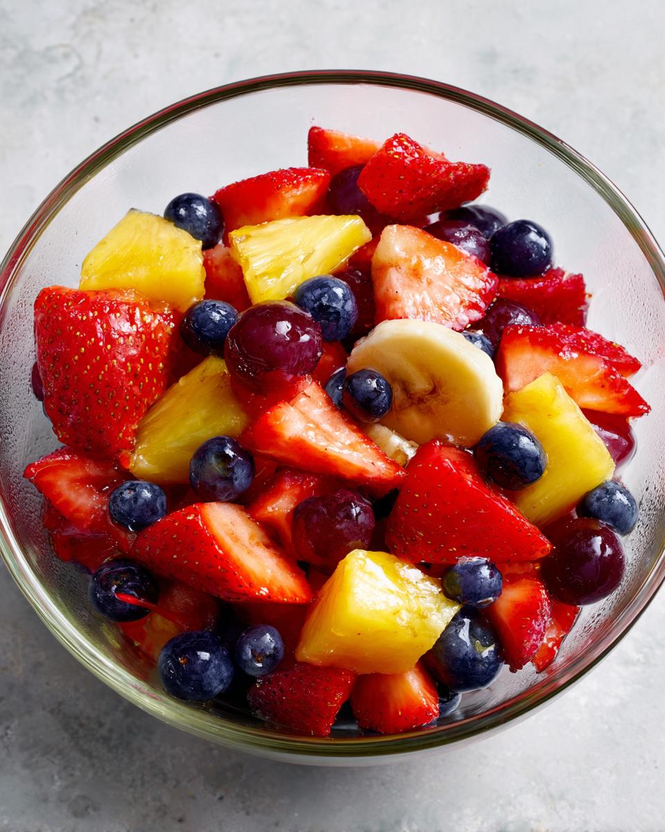 Colorful honey glazed fruit salad with strawberries, pineapple, blueberries, grapes, and banana slices