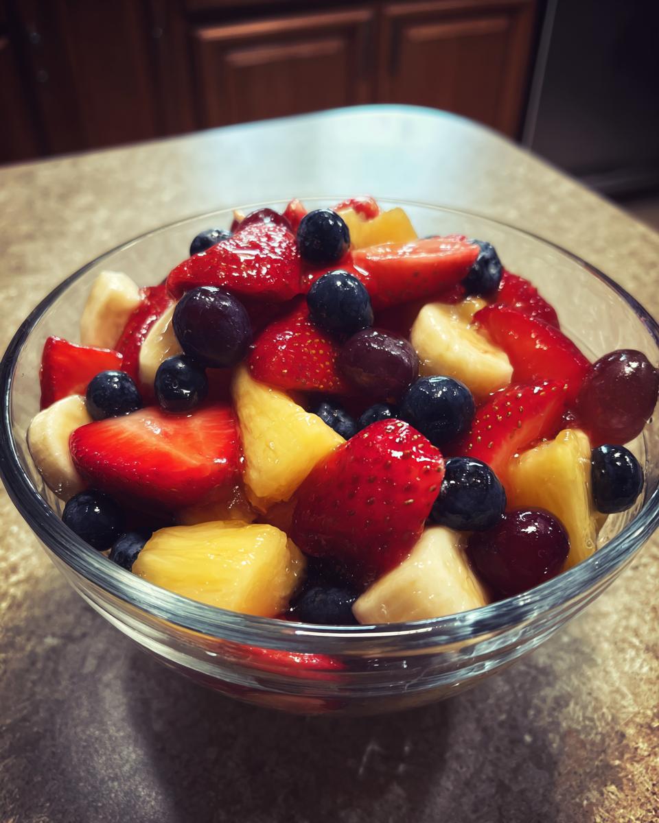 Close-up of a honey glazed fruit salad with strawberries, blueberries, pineapple, banana, and grapes.