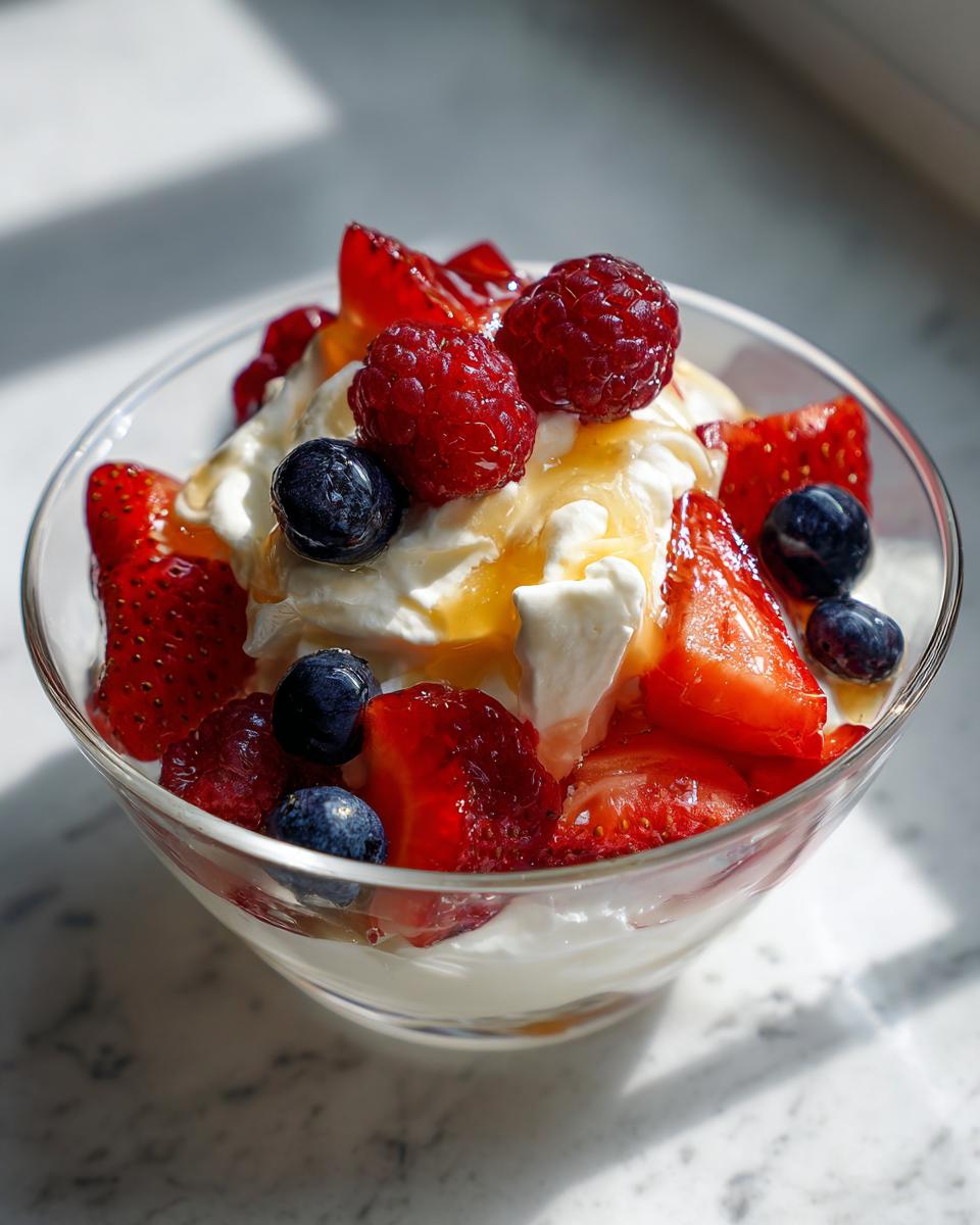 Glass bowl with mascarpone berry dessert recipe topped with raspberries, blueberries, strawberries, and honey